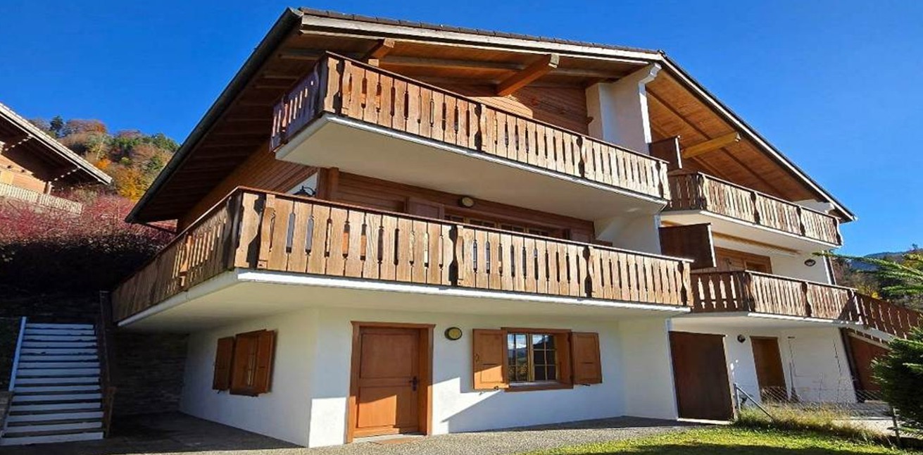Two story house, wooden balcony, red roof, two doors, one window, garden