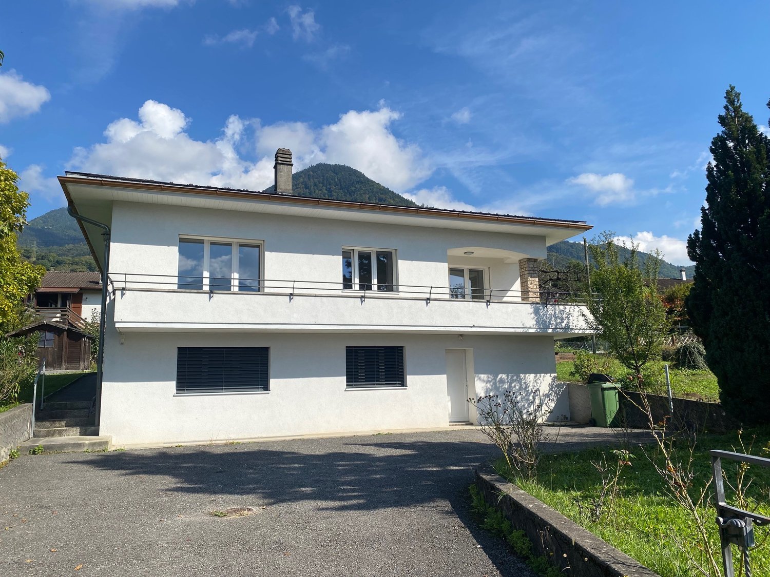 2-story house, white exterior, balcony on second floor, modern architecture, driveway, green grass, mountain backdrop