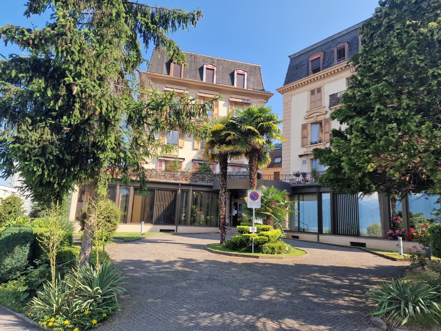 2 story building, beige paint, large windows, entrance with trees, palm tree, paved entrance