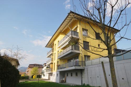 3 story yellow building, balconies on second and third floors, white exteriors, fenced area, grass, trees, mountains in distance