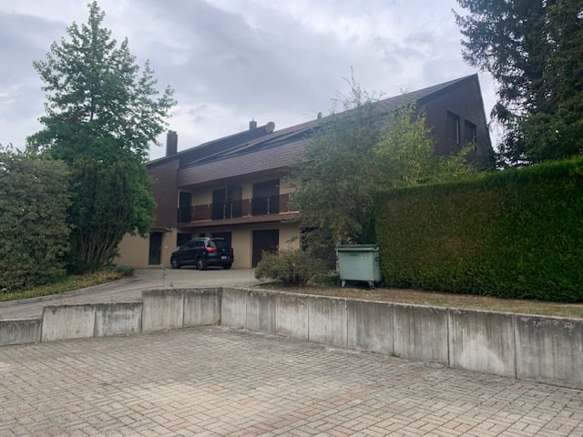 2-story brick building with a garage and parking space in the front, surrounded by trees and vegetation