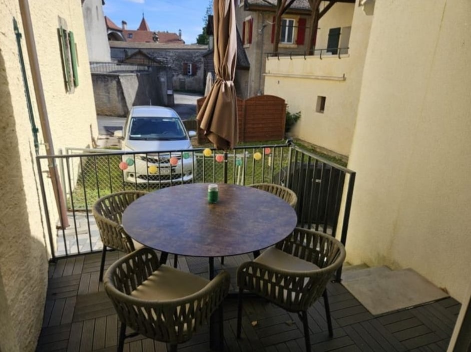 Balcony with table and chairs, car parked, umbrella, and colorful decor