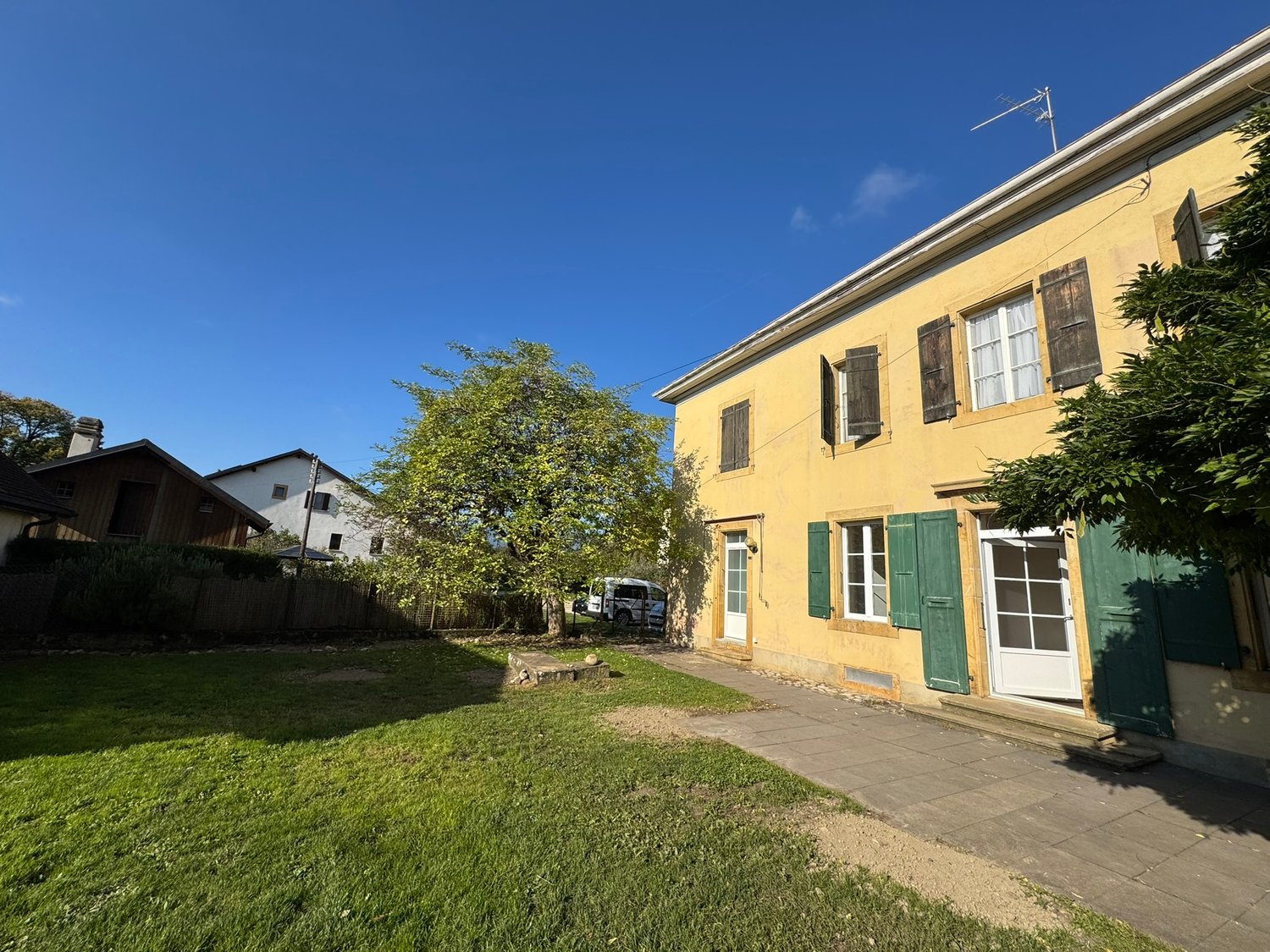 Large house, yellow paint, green shutters, stone path, fenced lawn, large tree
