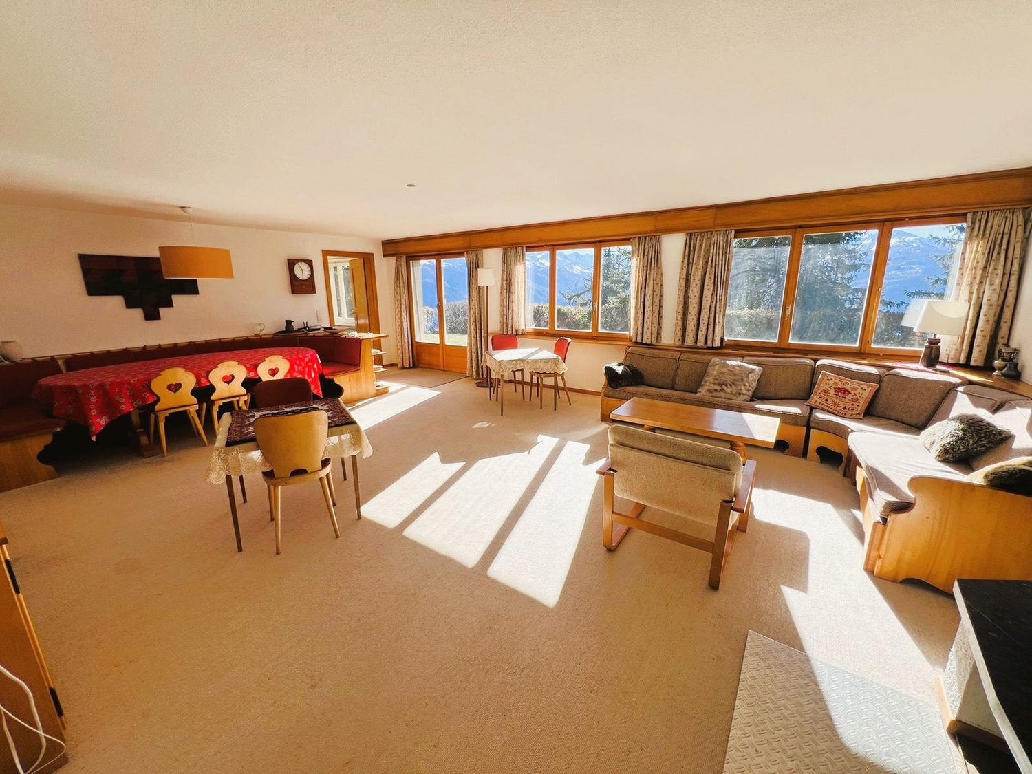 large living room with dining area, wooden furniture, large windows, carpets, picture frame on the wall