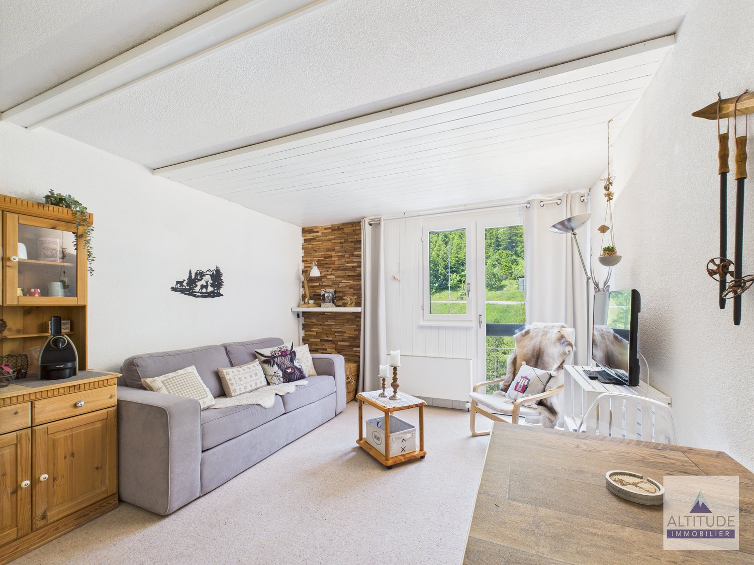Cozy living room with gray sofa, wooden shelves, brick accent wall, large windows overlooking a scenic outdoor view