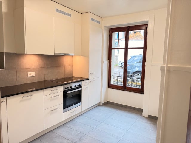 Kitchen with white cabinets, black countertop, oven, large window