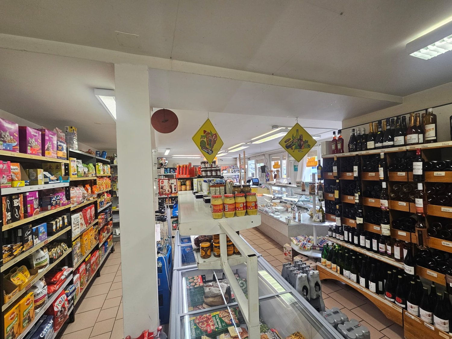 A grocery store with various products on shelves, including snacks, beverages, and condiments. There are also bottles of wine on the shelves.