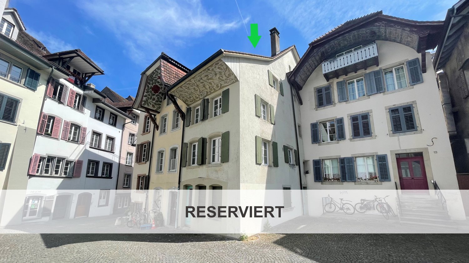Traditional European architecture, multiple floors, balcony, paved street, clear sky, multiple windows, bicycles parked outside, label reads 'RESERVIERT'
