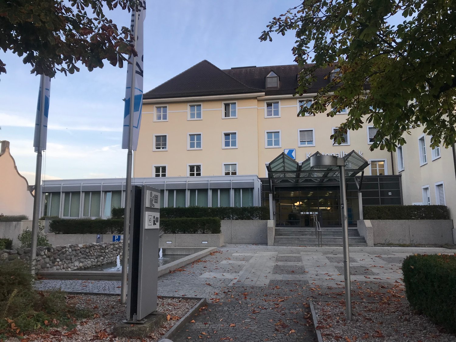 Building exterior with flags, yellow building, glass wall, stairs, plants, trees