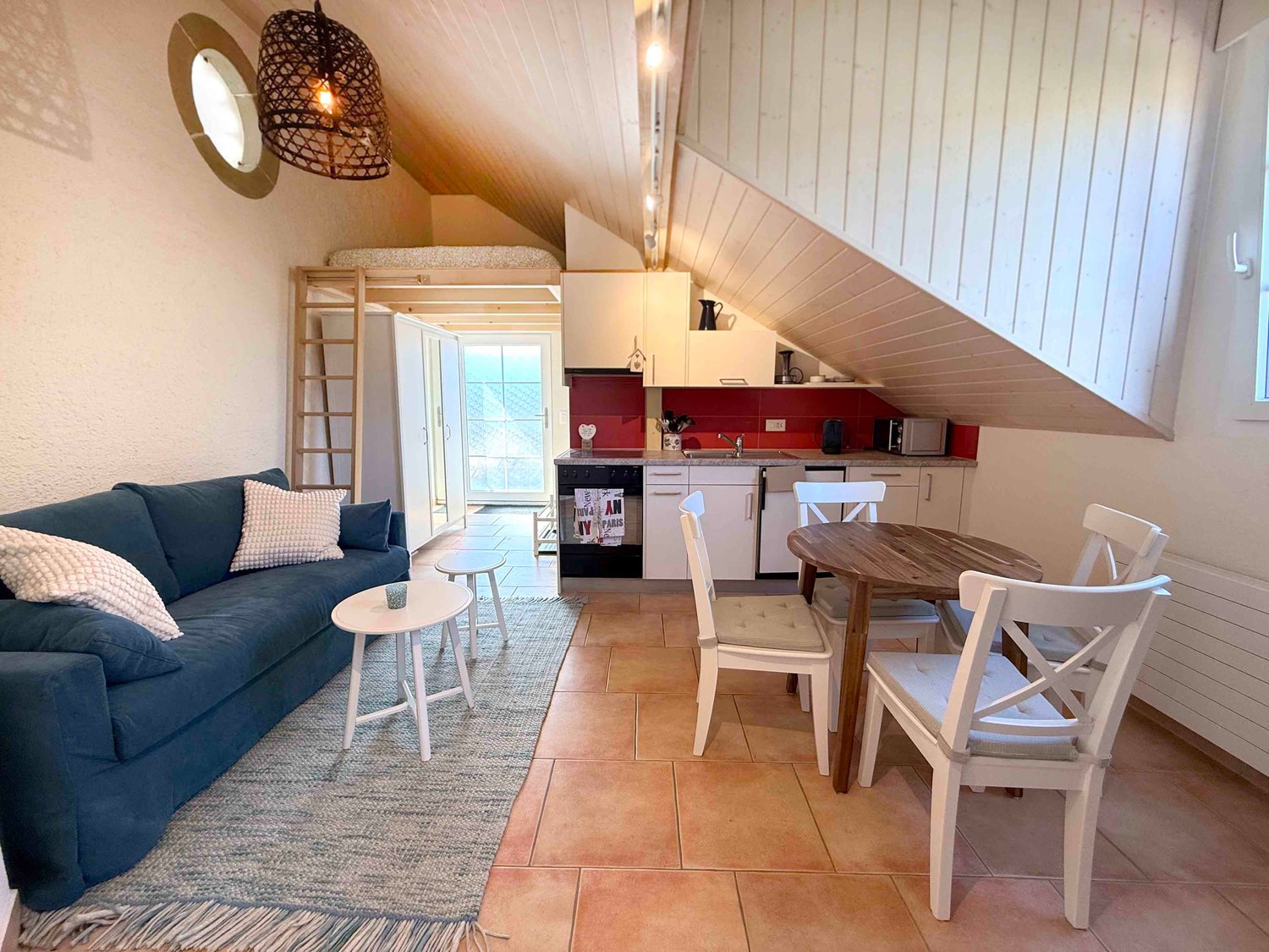 compact living room with dining area, sofa, coffee table, dining table with chairs, kitchen with sink, microwave, small window