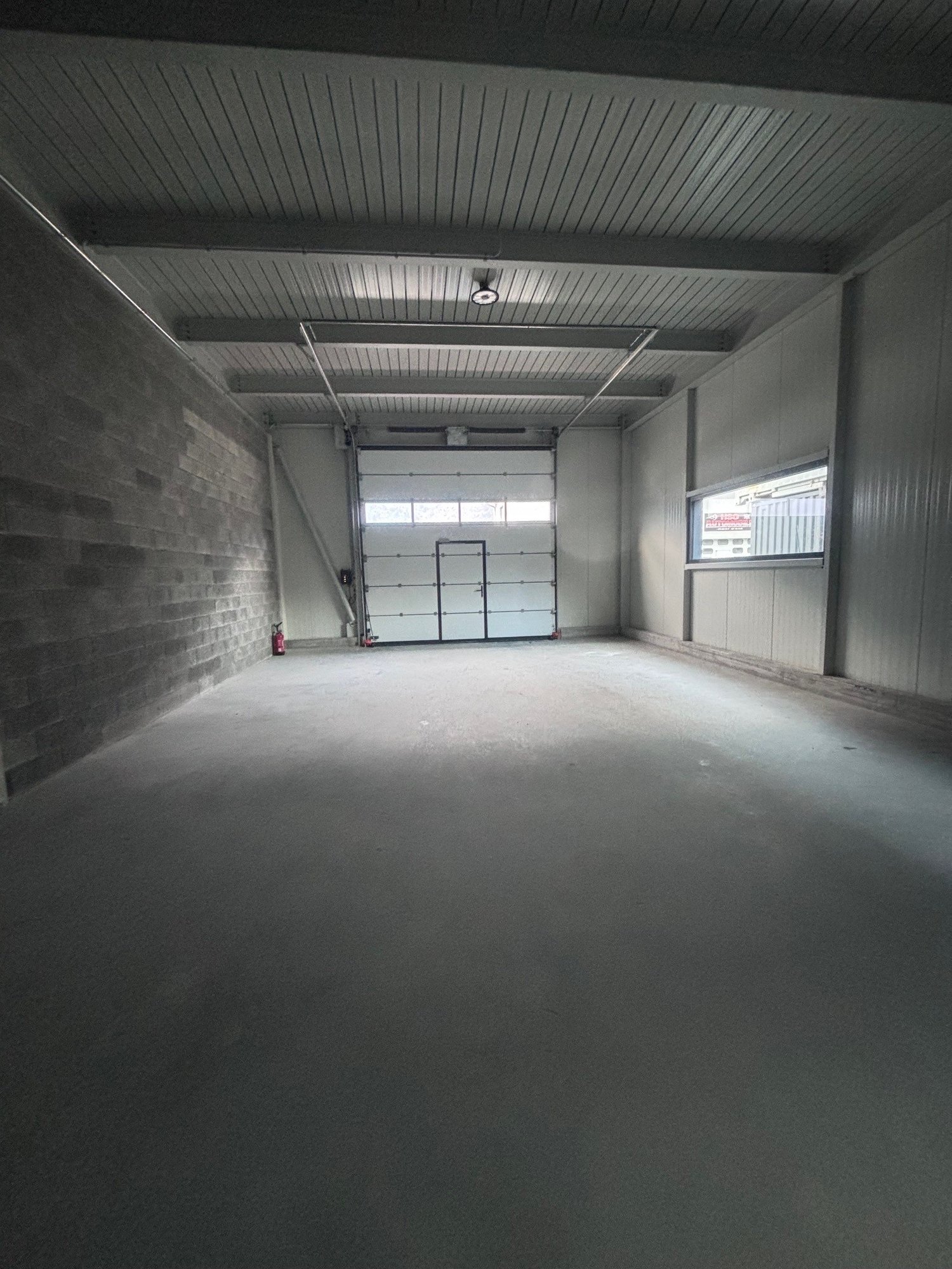 Empty room, industrial style, brick wall, white ceiling, overhead lighting, white door, fire extinguisher, window, wide open entrance