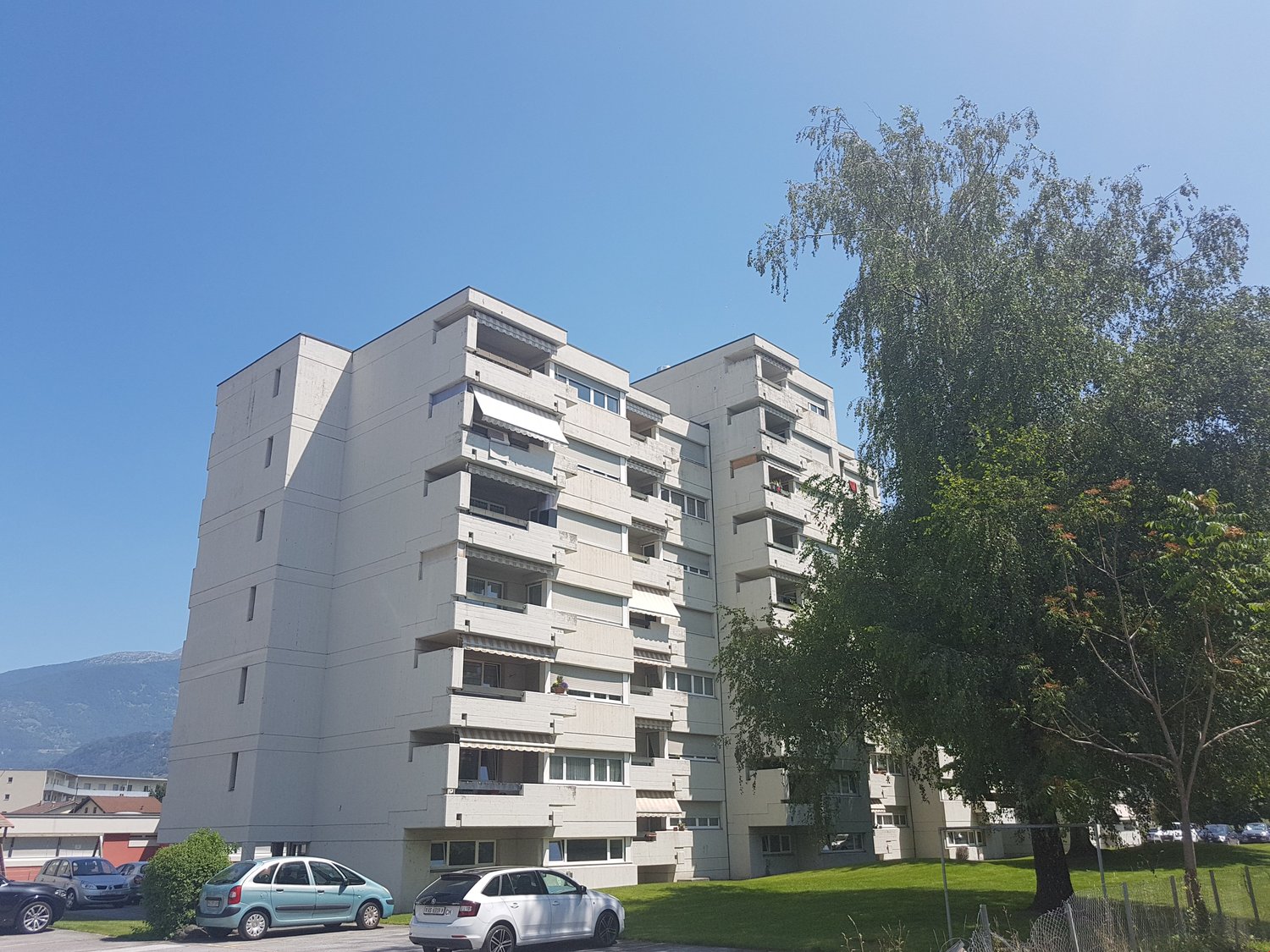 3-story building, white, balconies, cars parked in front