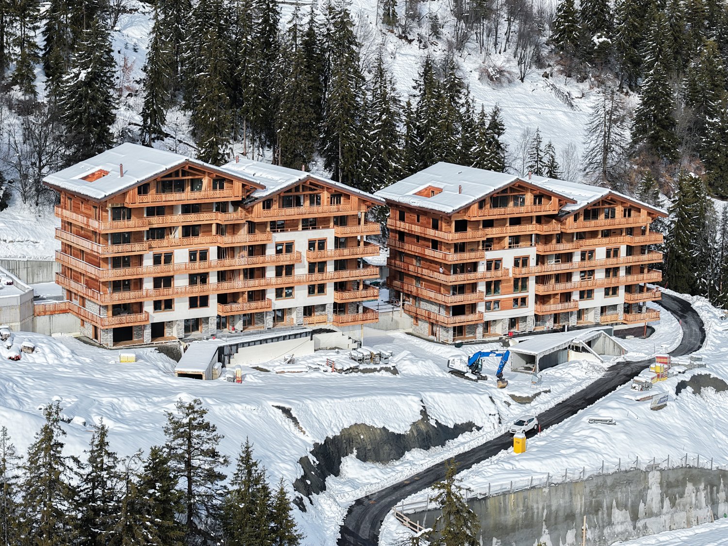 Two wooden apartment buildings, multiple floors, balconies, snow-covered surroundings, under construction