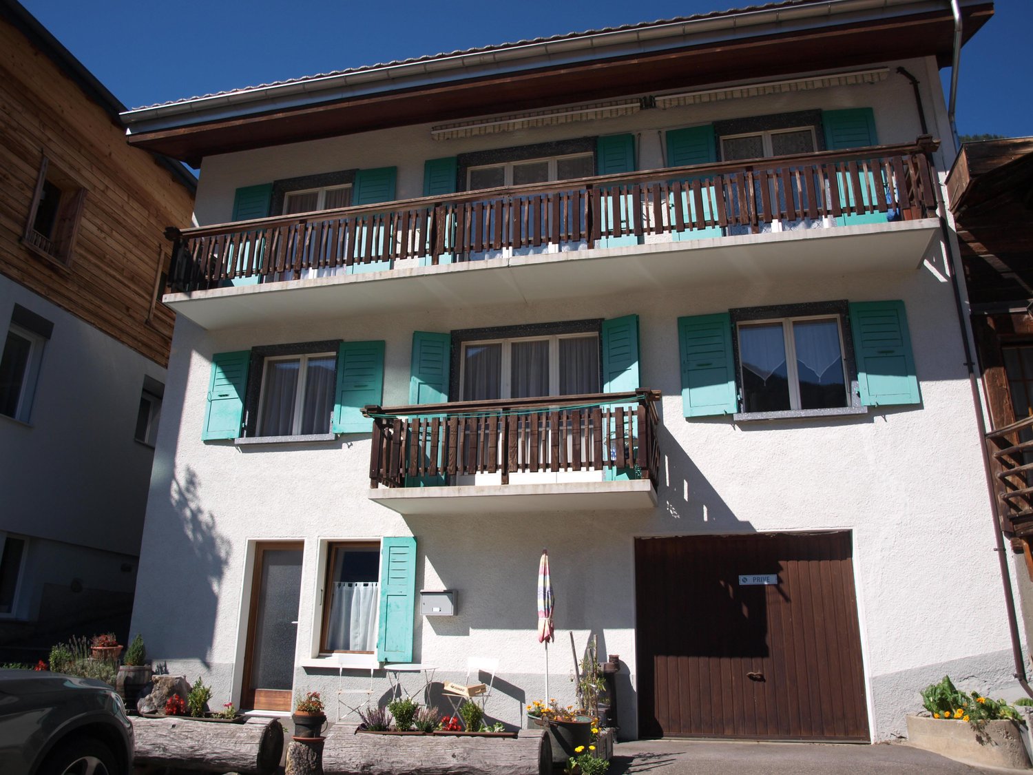 2-storey house with turquoise shutters, wooden garage door, 2 balconies, greenery around