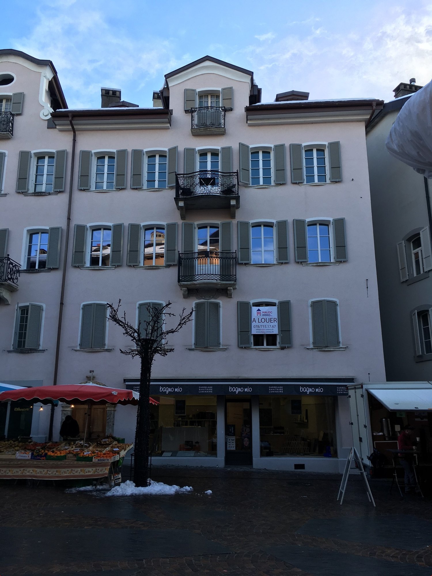 white building with many windows, balcony, multiple floors, red awning outside