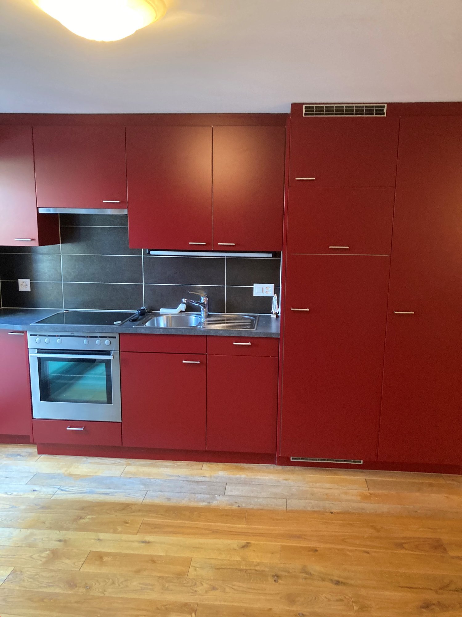 Modern kitchen with red cabinets, gray countertops, stainless steel sink, dishwasher, integrated oven and stove