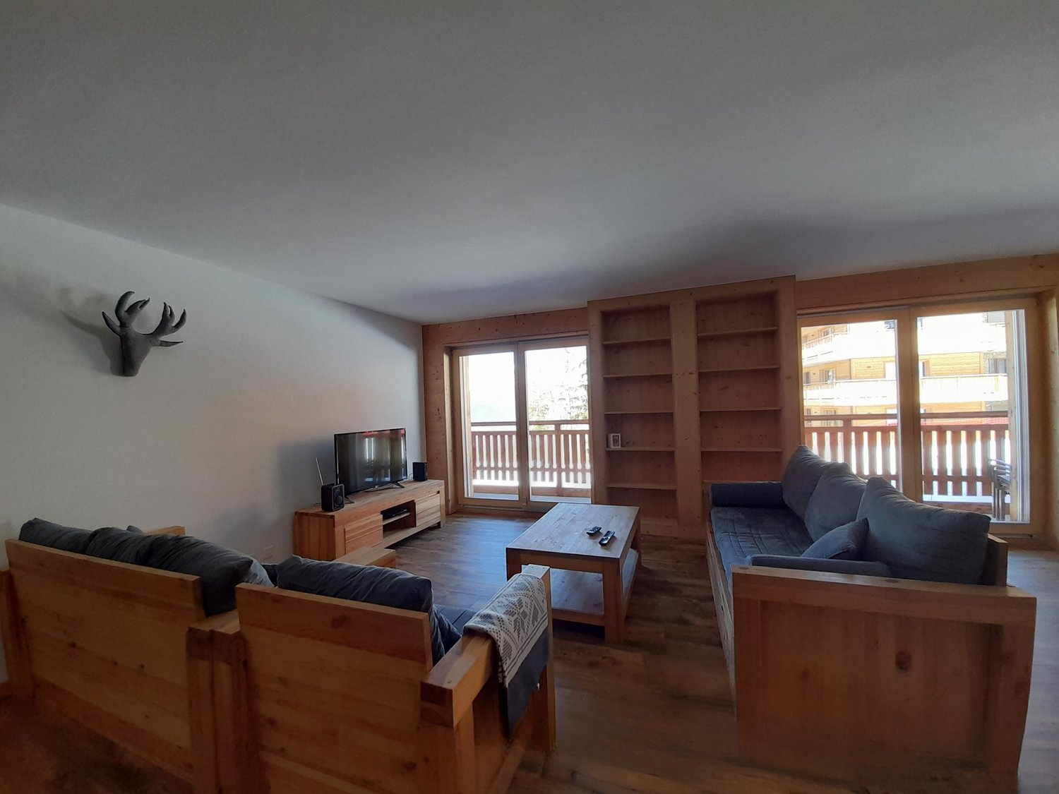 wooden furniture, wooden floor, TV, coffee table, large windows with balcony, wooden cabinet