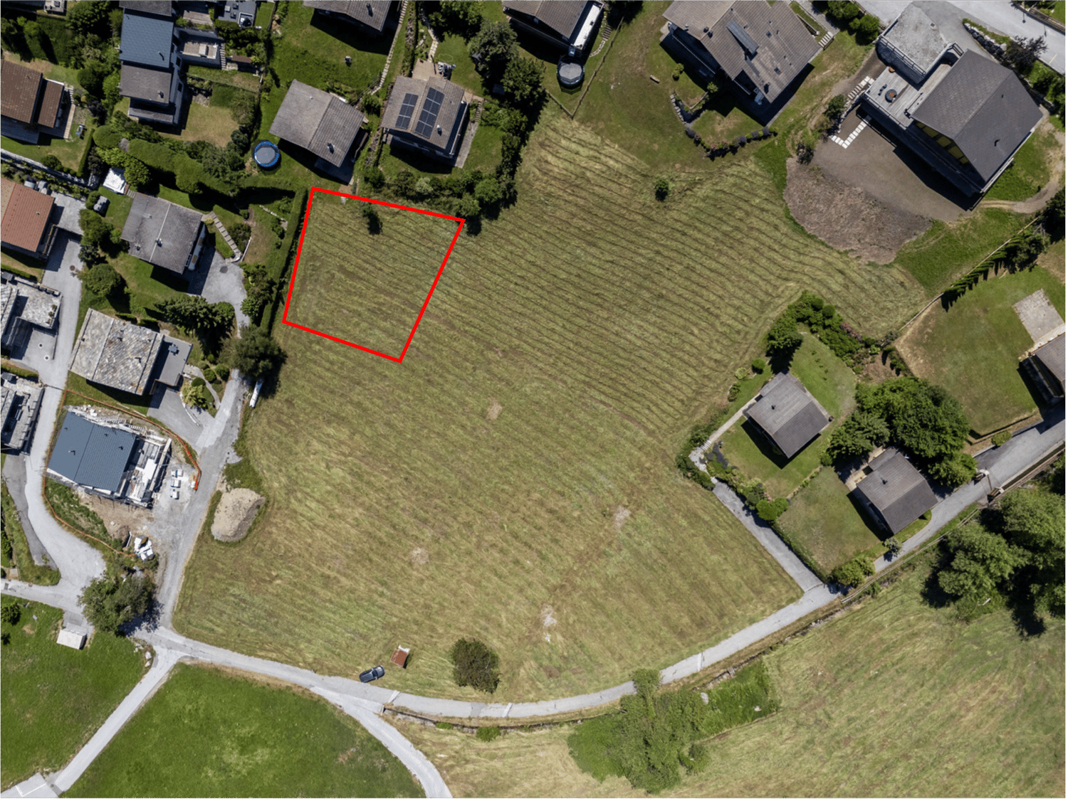 Aerial view of a plot of land with surrounding houses and green areas.