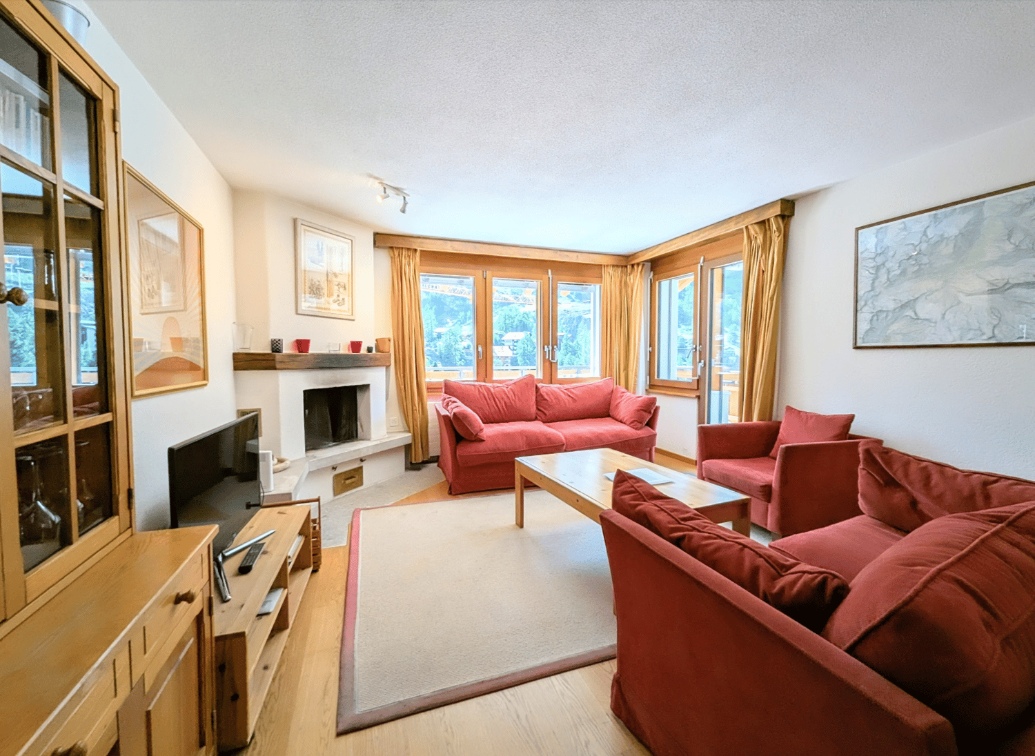 Spacious living room with large windows, red sofas, wooden furniture, and a fireplace