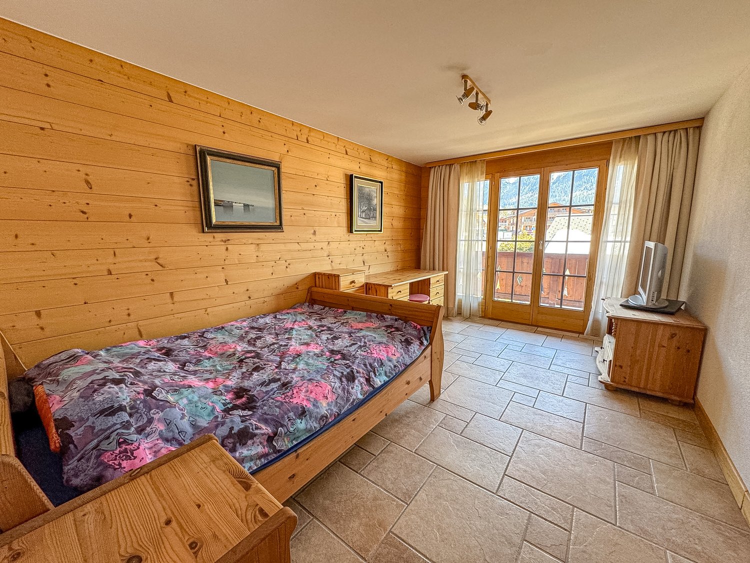 wooden walls, bed, desk, TV, glass doors, tiled floor