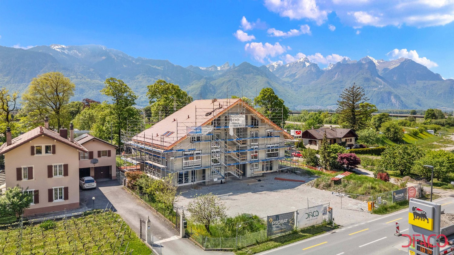 Building under construction, surrounded by greenery, with mountains in the background