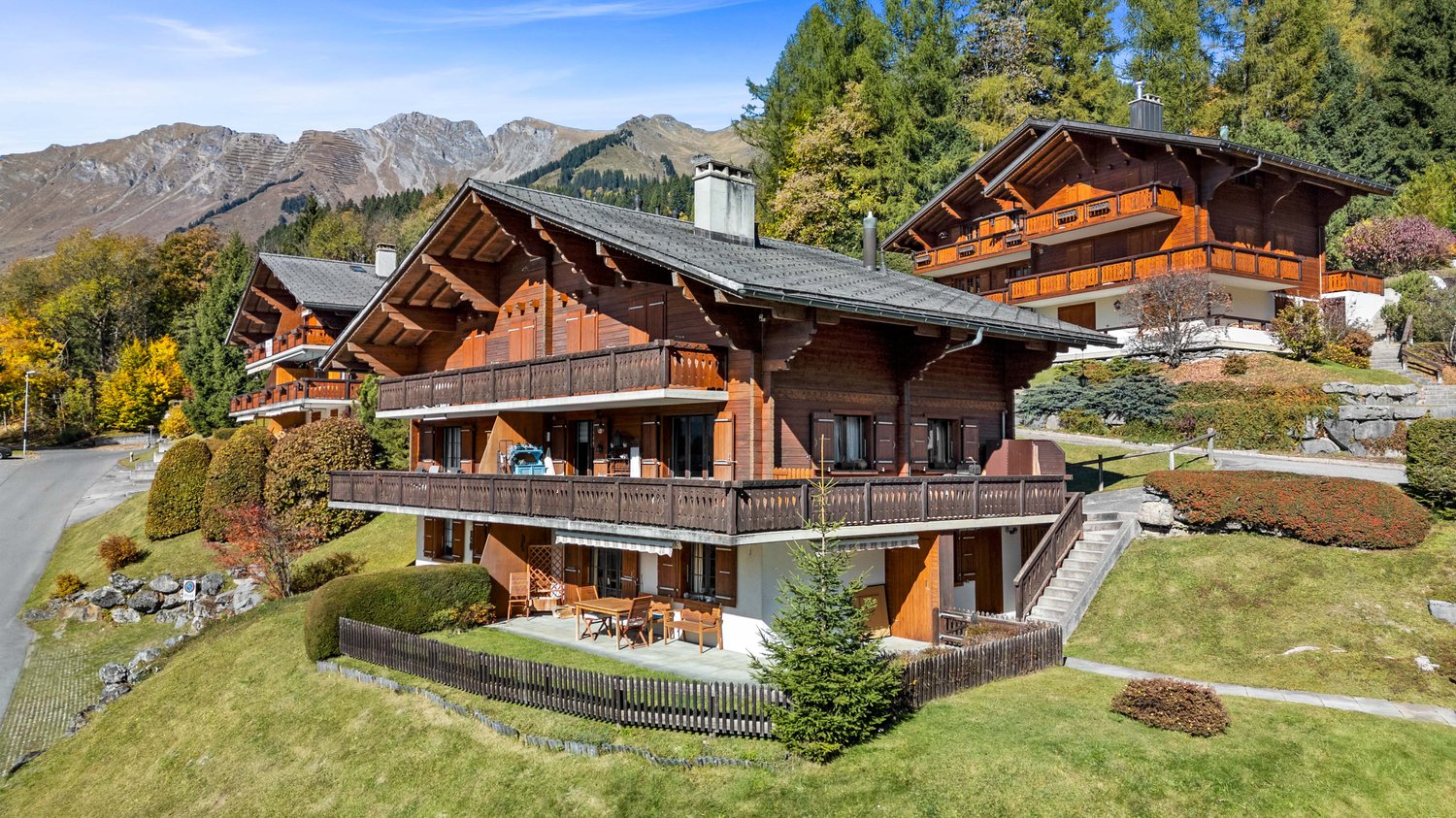 large chalet, wooden exterior, balcony, lawn, terrace, surrounded by trees