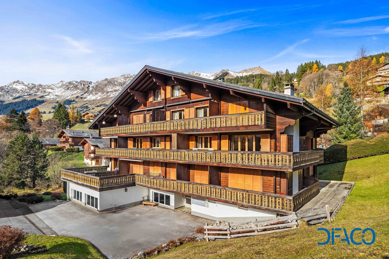 large chalet-style wooden house, multiple balconies, snow-covered mountains in background