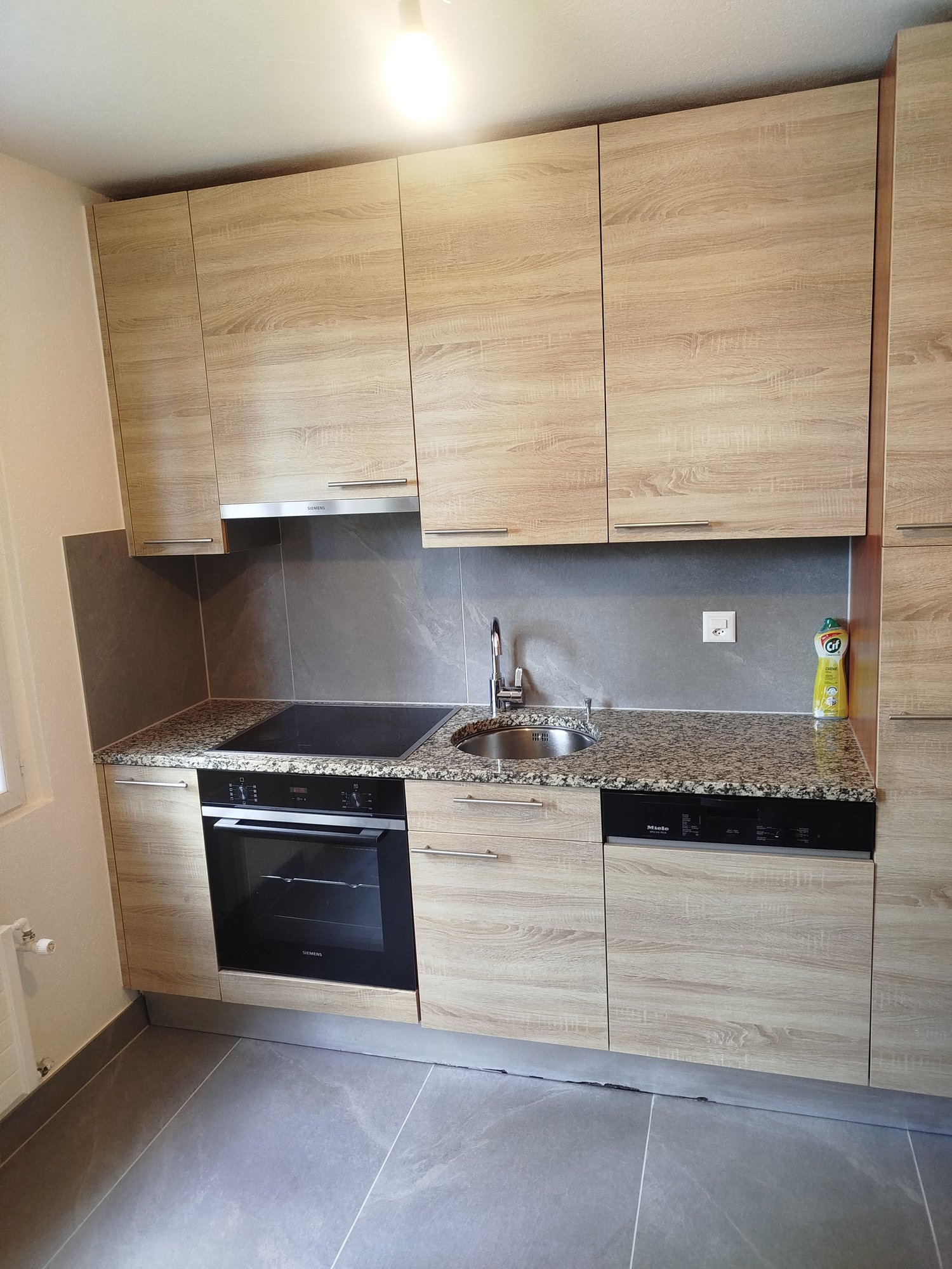 modern kitchen, light wood cabinets, granite countertop, black stove, stainless steel sink, dishwasher, silver faucet, built-in lighting