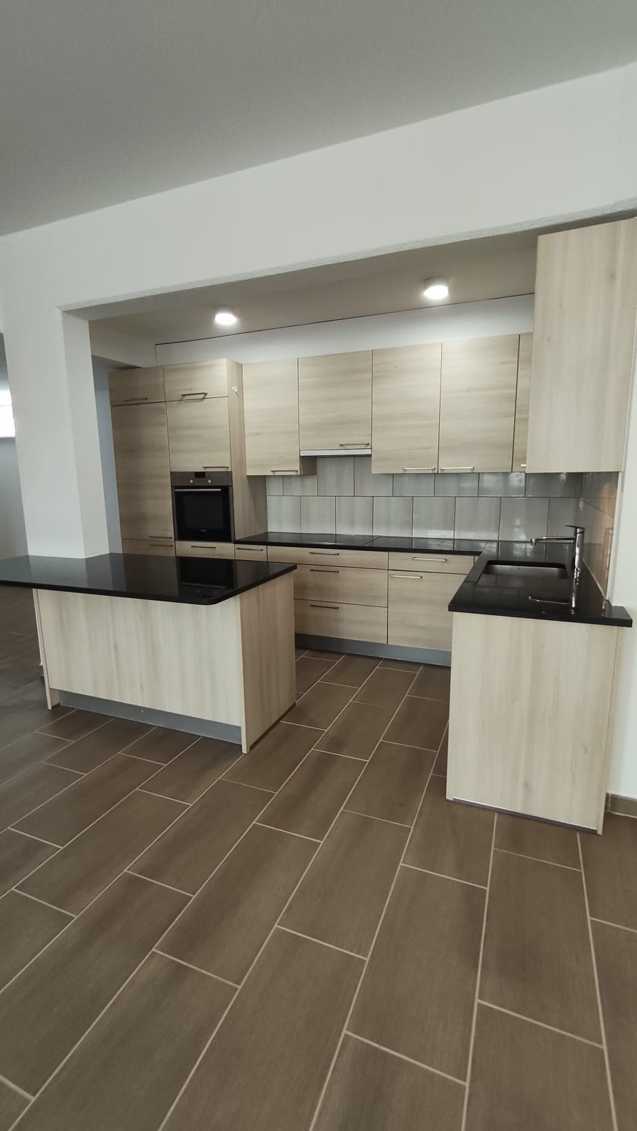 modern kitchen with wooden cabinets, black countertops, tiled floor, built-in oven, dishwasher, sink
