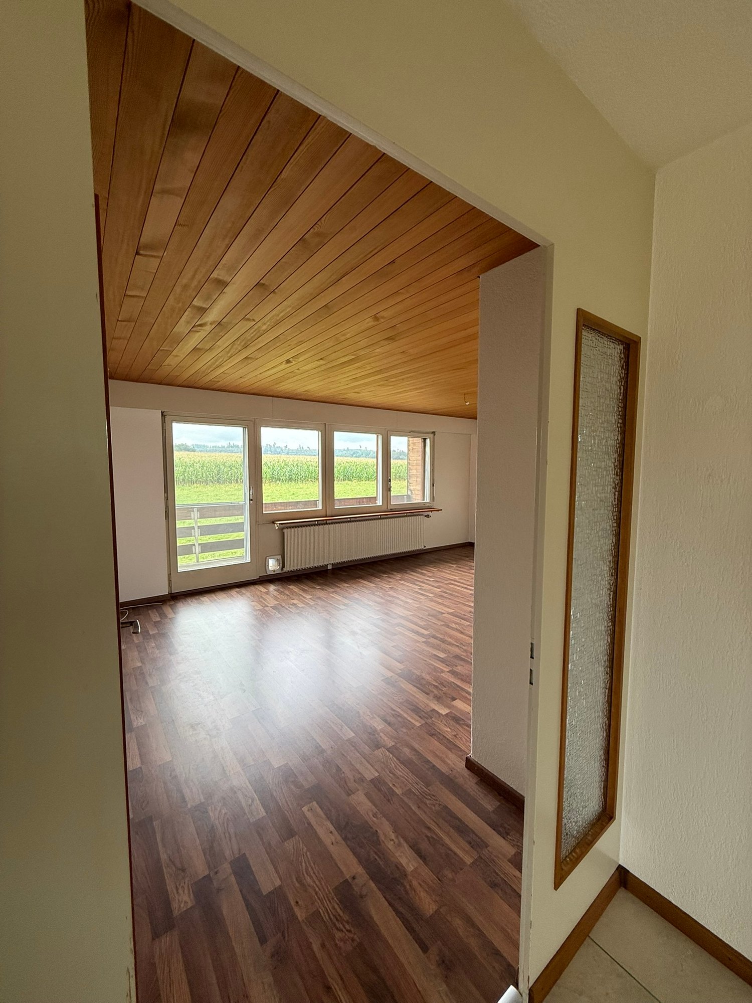Empty room with wooden floors, large windows, and wooden ceiling, with scenic view.