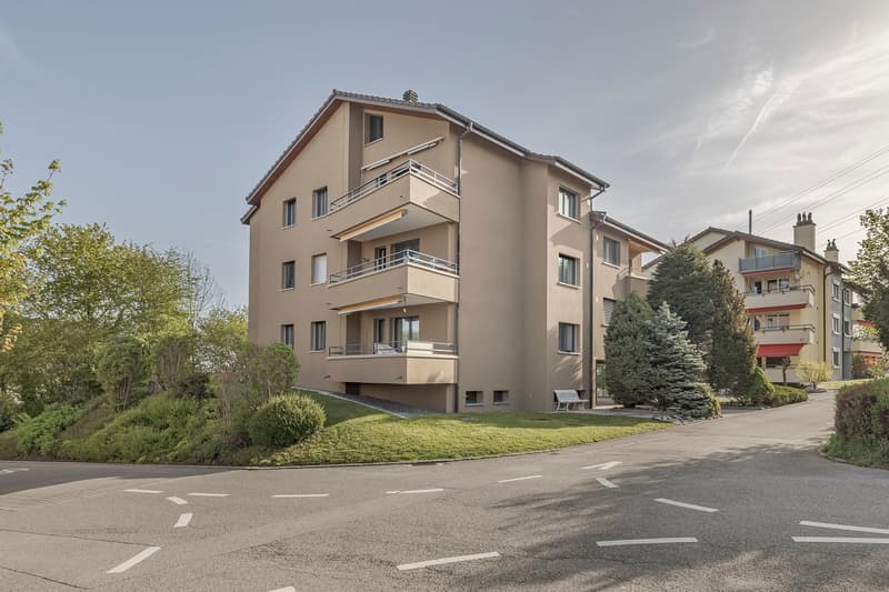 Three-story apartment building with balconies and greenery.