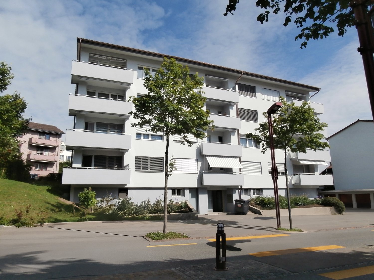 apartment building with white balconies, grey exterior, small garden in front