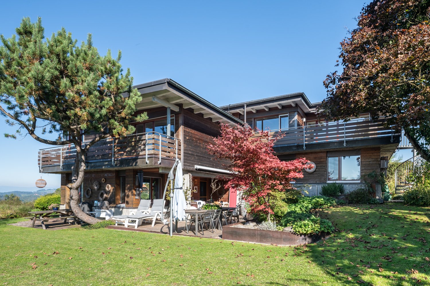 modern two-story house, wooden exterior, balcony, open-air dining area, lawn, mountain view