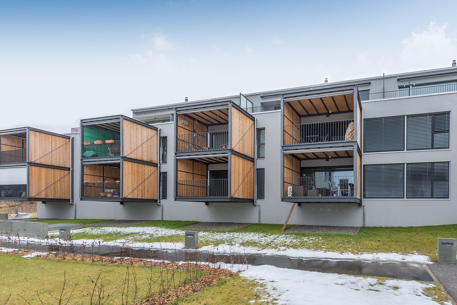 modern apartment building, glass windows, wooden balconies, snow on ground