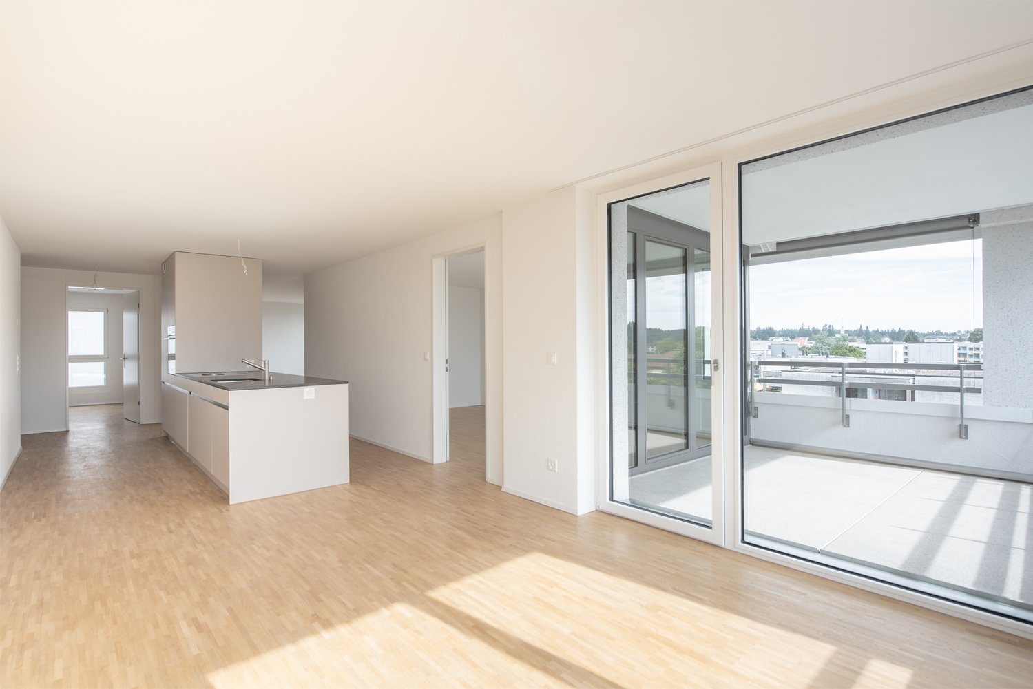 empty room with kitchen, balcony with sliding doors, wooden floor