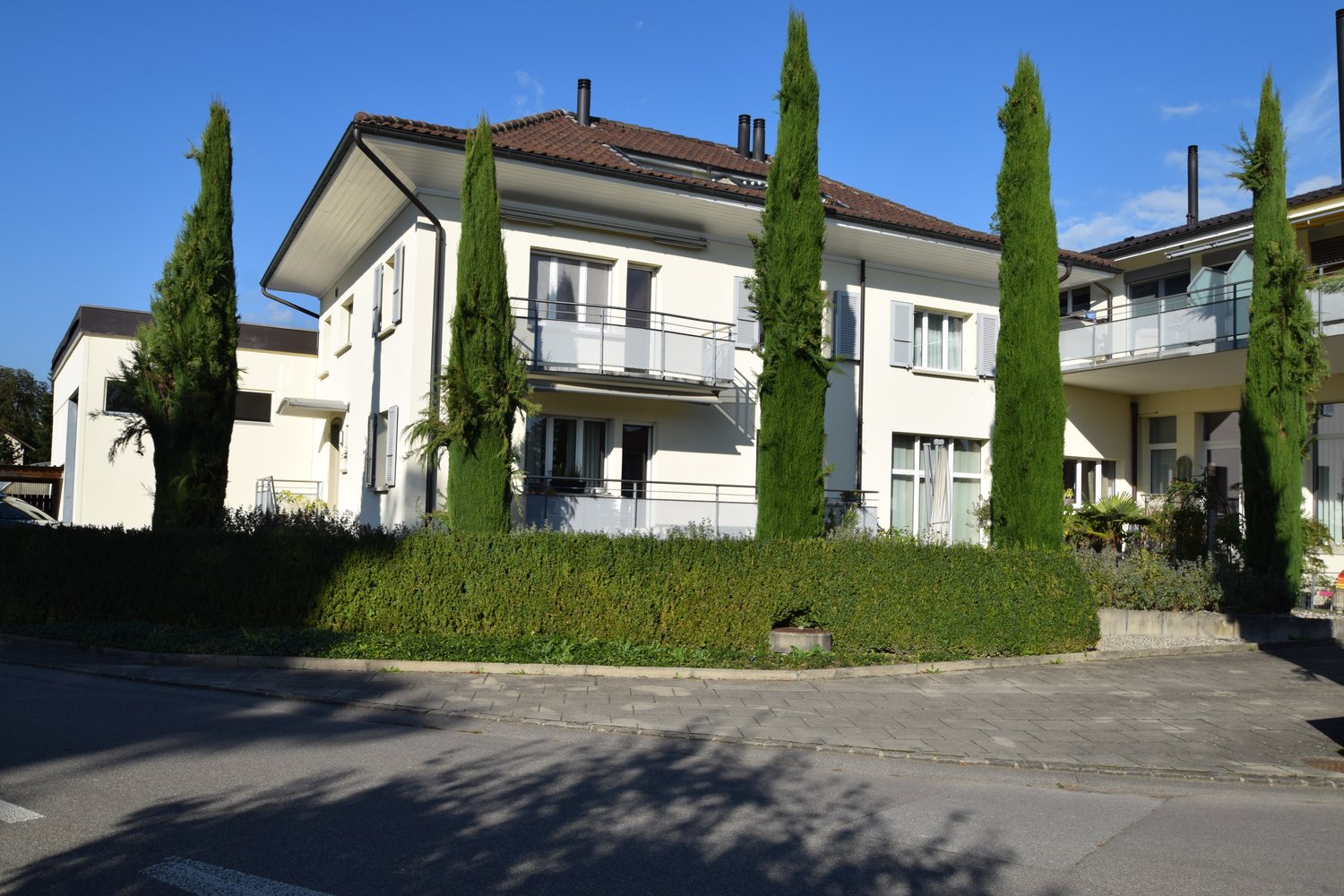 3 story white house, brown roof, windows, balconies