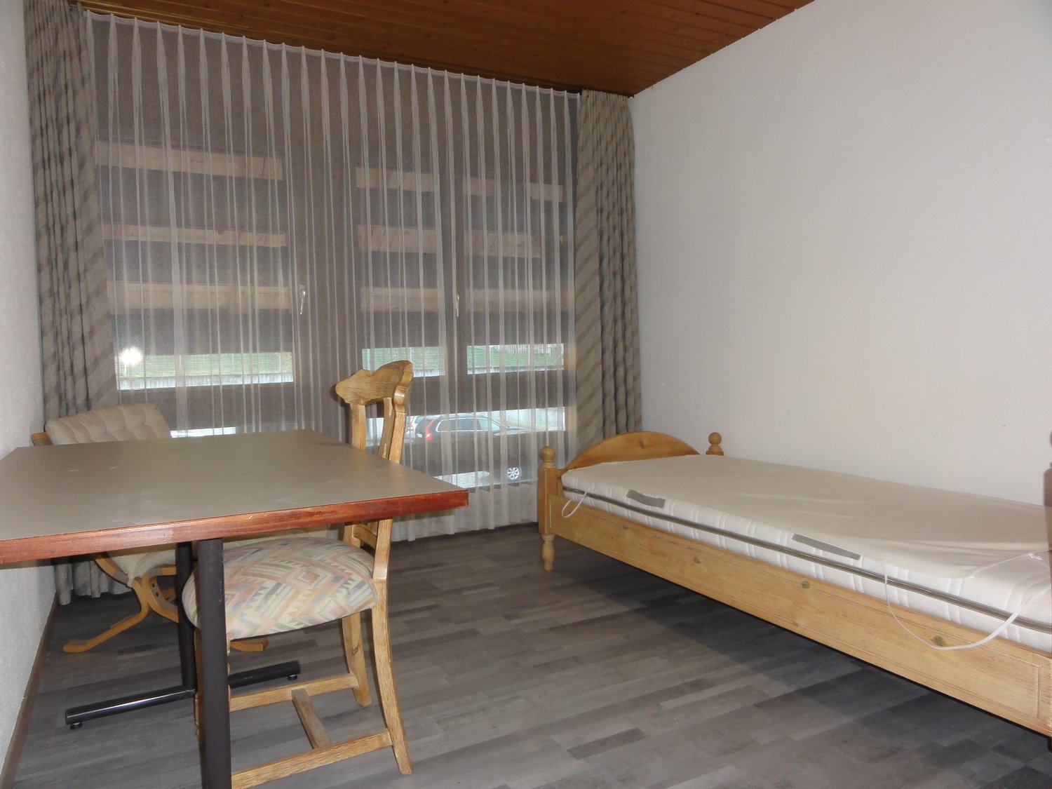 Bedroom with bed, desk and chairs, light colored wood flooring