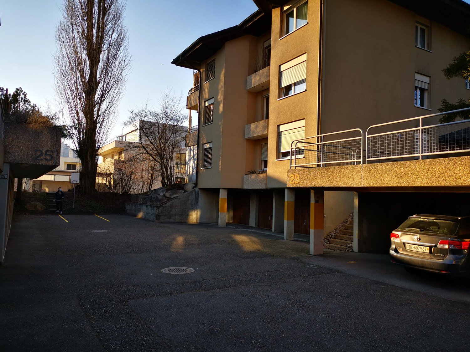 Residential building with multiple units and a garage entrance on the ground floor. Stairs are located on the left side. The building has beige and brown colors.