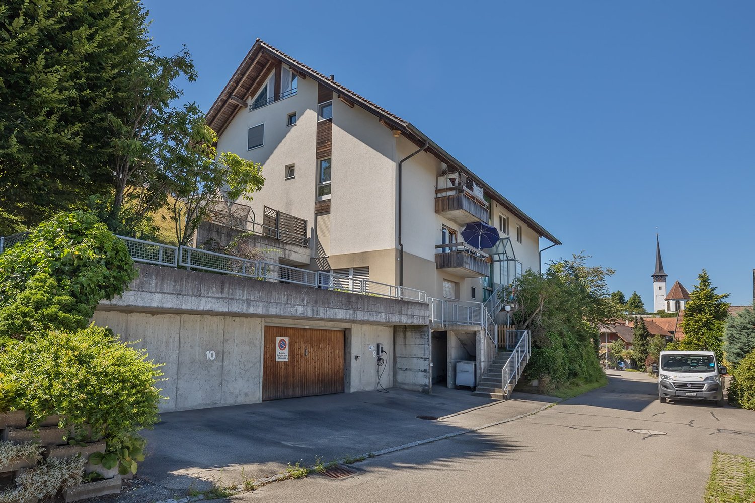 2 story building, beige and white walls, wooden entrance door, electrical charging station, balcony, fenced entrance with stairs