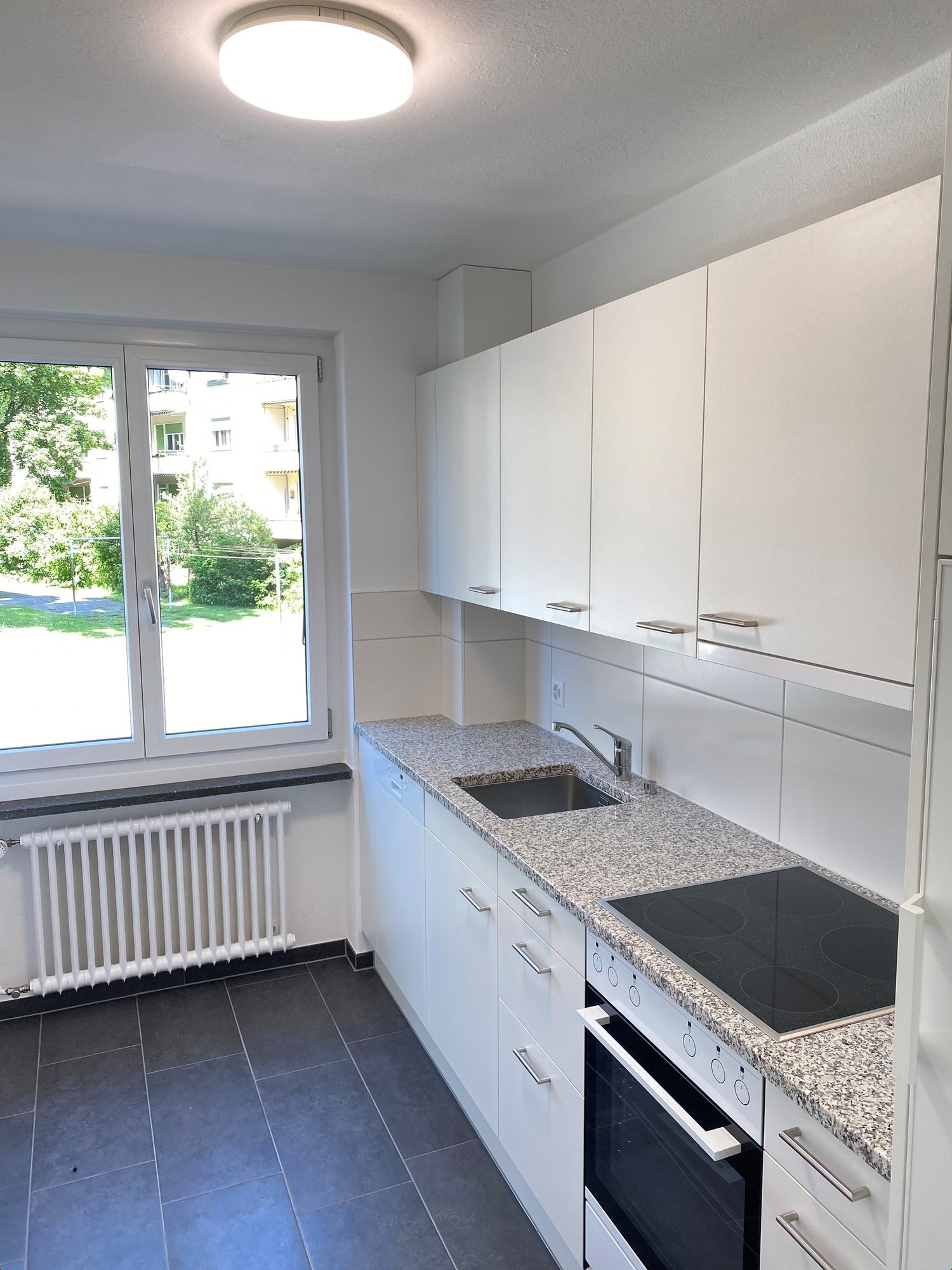 modern kitchen with ceramic countertops, white cabinets, electric stove, oven, sink, faucet, underfloor heating, large window