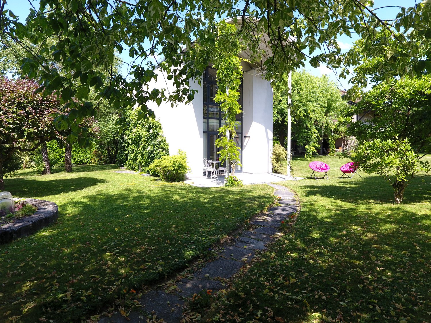 Contemporary house, white walls, glass windows, pathway, garden with green grass, trees, pink lounge chairs
