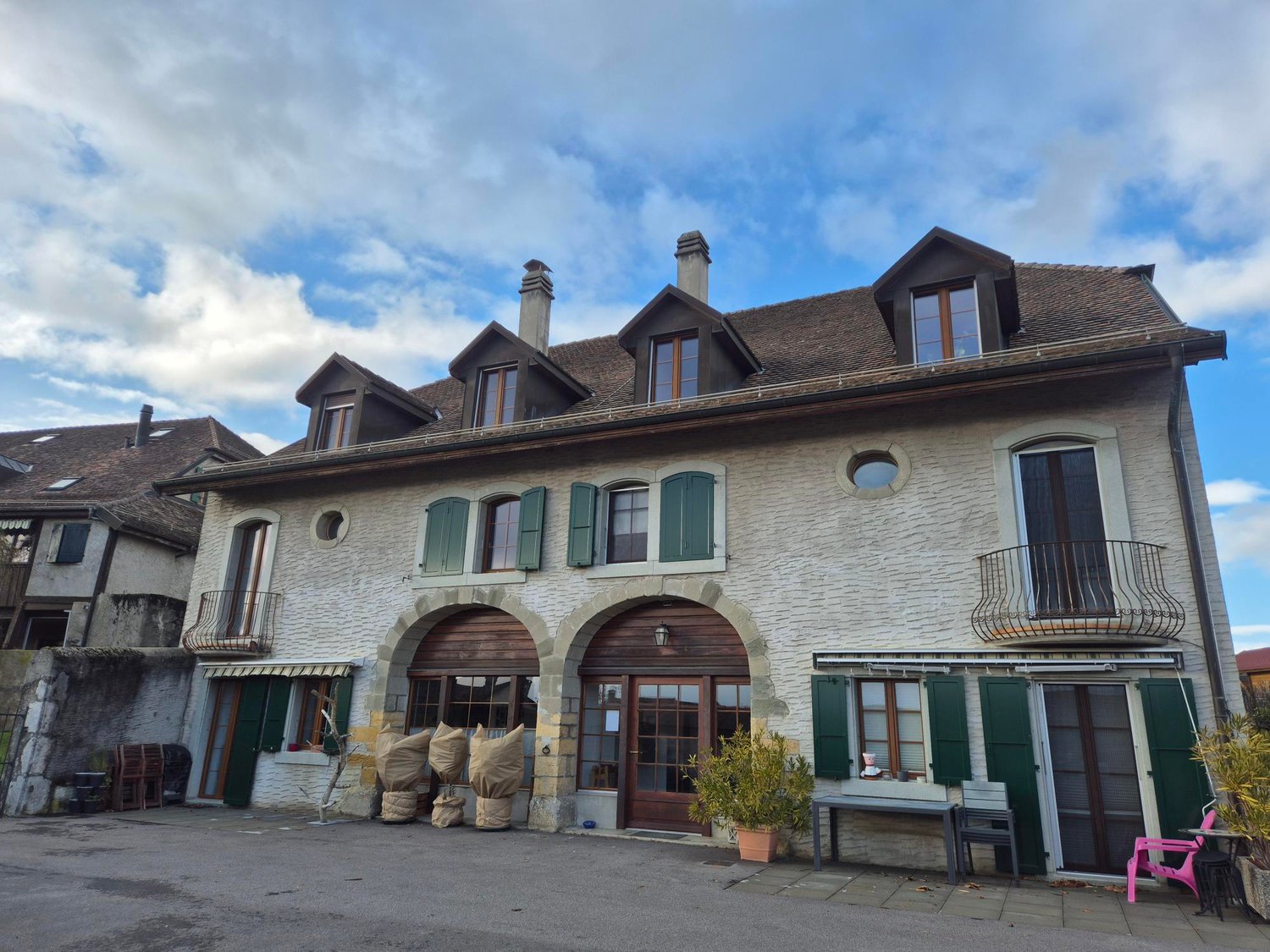 Stone exterior, brown roof, multiple arched entrances, green shutters, balcony, chimneys