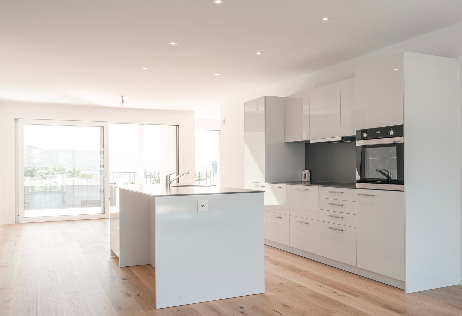 white cabinets, wooden floor, island countertop, sink, faucet, oven, refrigerator, built-in appliances, double glass doors leading to balcony