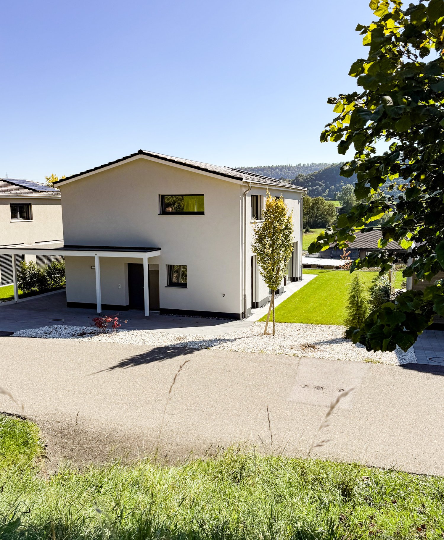 Modern white house, 2 stories, concrete driveway, driveway carport, tree, lawn, distant house and mountain