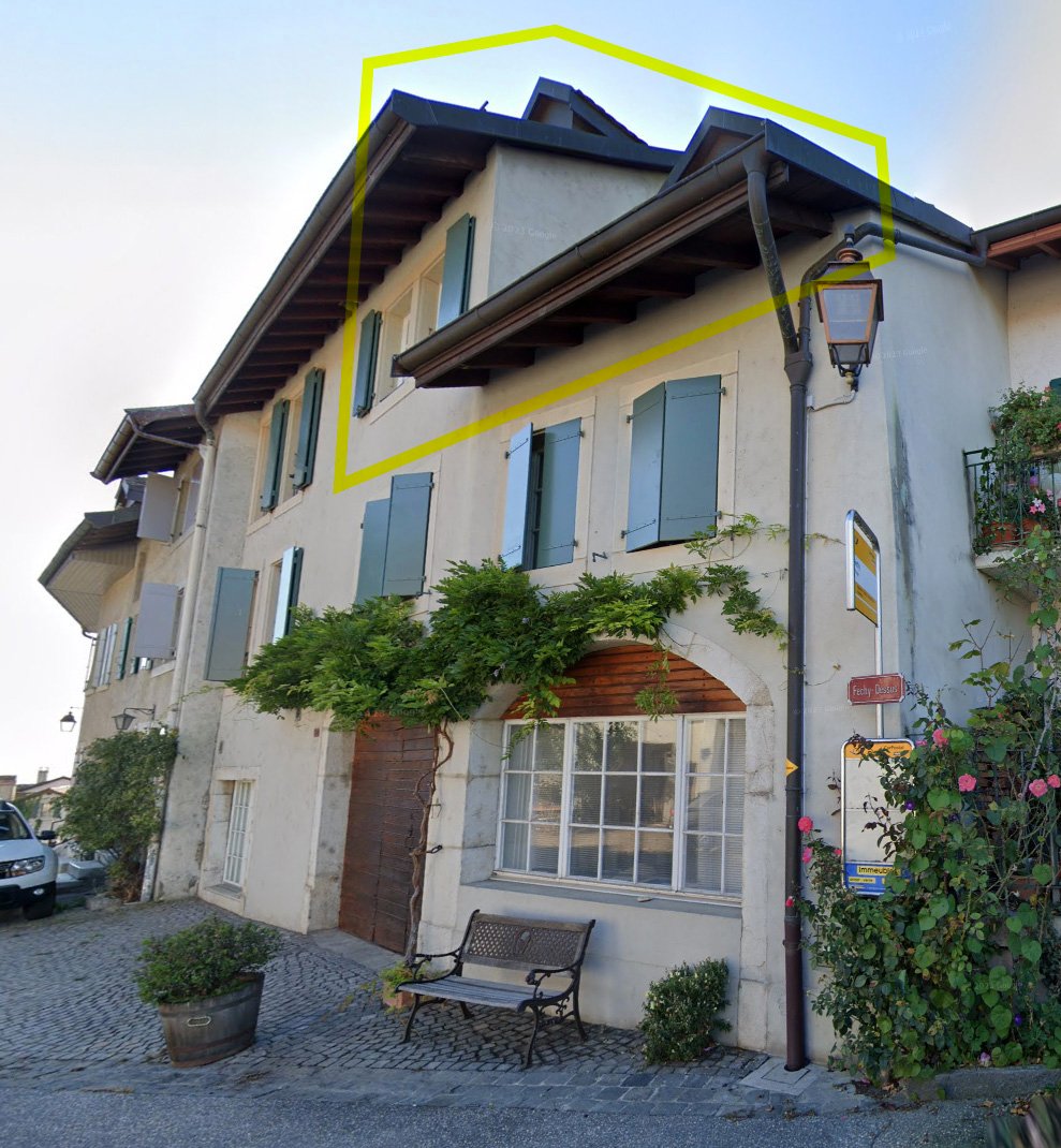 2-story building with a traditional European architectural style, featuring wooden beams, shuttered windows, and a covered entryway. The building has a balcony or terrace on the upper level.