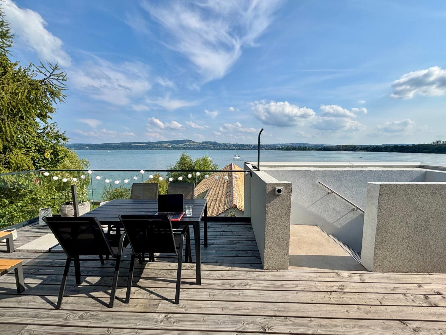 Wooden deck with tables and chairs, outdoor glass railing, view of a lake