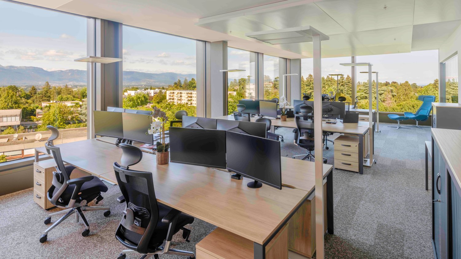 Large windows, desks, monitors, office chairs, trees and mountains view outside