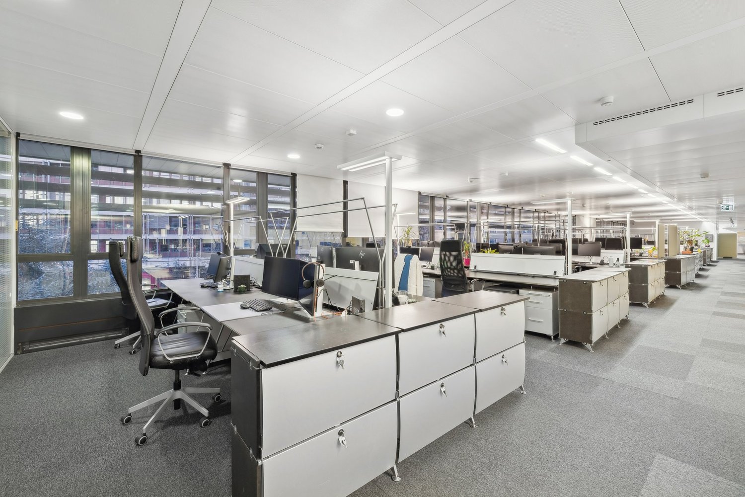 modern office layout with desks, black office chairs, monitors, keyboards, large windows