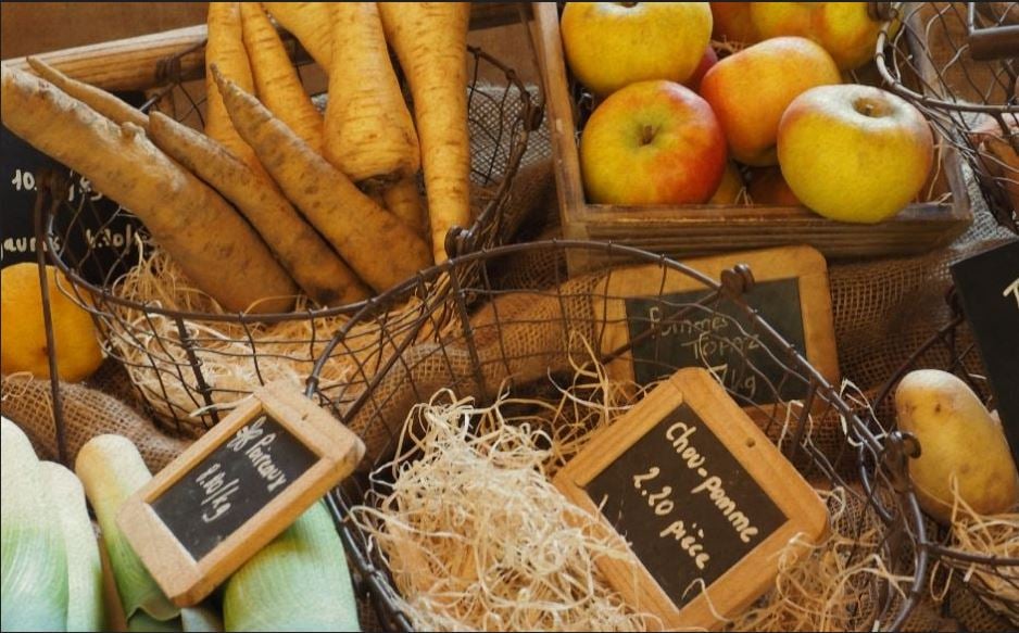 Various fresh produce including parsnips, apples, potatoes, leeks, and lemons in baskets with wooden labels