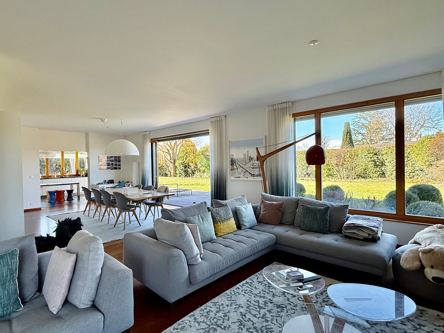 large L-shaped sofa, glass tables, carpet, large windows, glass sliding door, garden view